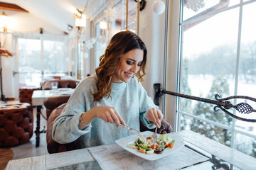 Smiling woman eating fresh salad in restaurant - Powered by Adobe