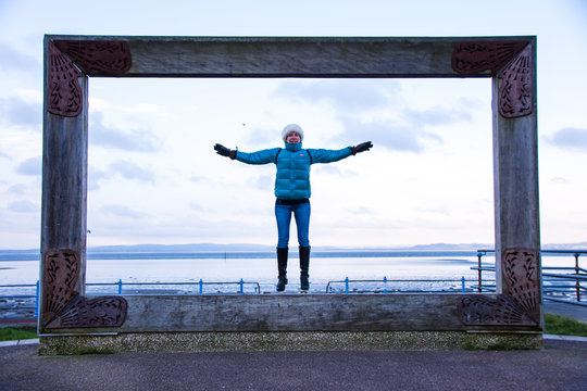 Model in big picture frame at Morecambe seafront jumping and having fun