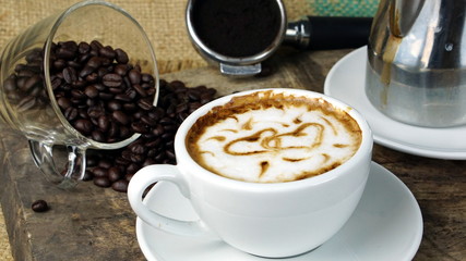Cappuccino coffee. A cup of latte, cappuccino or espresso coffee with milk put on a wood table with dark roasting coffee beans. Drawing the foam milk on top.