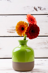 Enameled vase with gerberas. Flowers in vase on wood. How to grow plants. Beautiful items of room design.