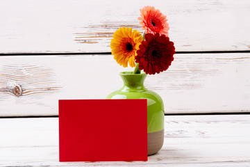 Blank paper near gerberas. Card, flowers, and ceramic vase. Congratulate with handwritten card. Space for imagination.