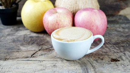 Cappuccino coffee and fruits. A cup of latte, cappuccino or espresso coffee with milk put on a wood table with dark roasting coffee beans. Drawing the foam milk on top.