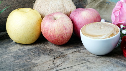 Cappuccino coffee and fruits. A cup of latte, cappuccino or espresso coffee with milk put on a wood table with dark roasting coffee beans. Drawing the foam milk on top.