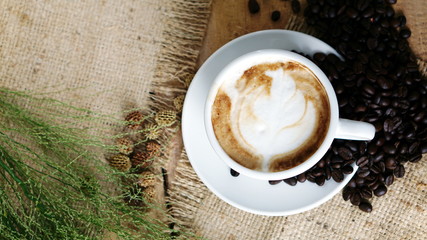 Cappuccino coffee. A cup of latte, cappuccino or espresso coffee with milk put on a wood table with dark roasting coffee beans. Drawing the foam milk on top.