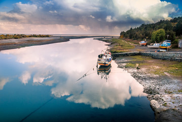 Fishing boat in the reflection of the cloud on the river by the ocean, Aytuy, Chiloe island, Chile, South America