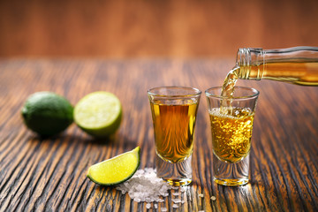 Pouring  tequila shot with lime on a  brown wooden background ,s