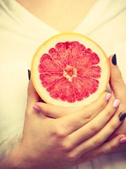 Woman holds half of grapefruit citrus fruit in hand