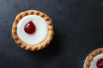 Cherry bakewell tarts in foil cases on dark background