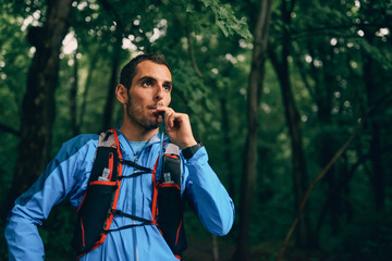 Fit male jogger hydrates while day training for cross country forest trail race in a nature park.