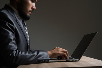 Young businessman sitting working with laptop isolated on black.