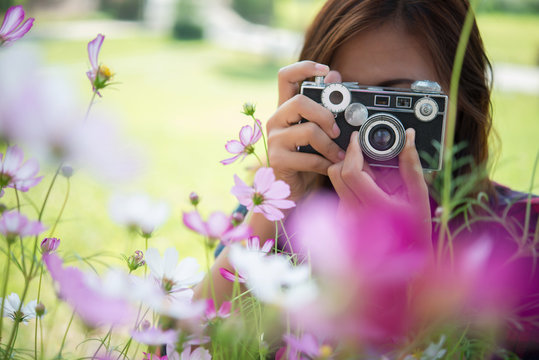 Hipster girl with vintage camera focus shooting flowers at park.