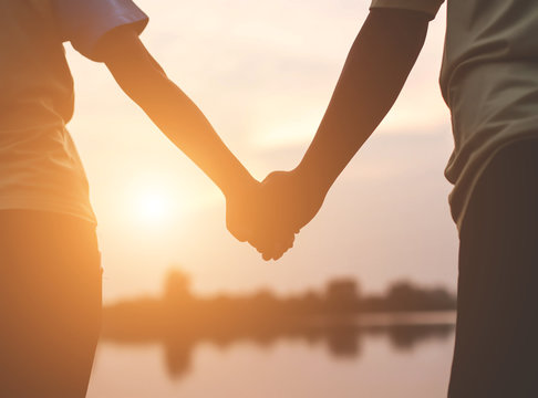 Closeup silhouette of loving couple holding hands while walking at sunset 