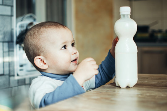 Beautiful Baby Reaching For Milk That Is On The Table In The Plastic Bottle