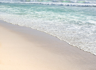 Gentle wave ripples of aqua blue ocean on sandy beach 