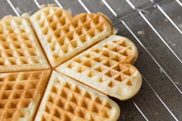 Freshly backed waffles in shape of heart, resting on metal rack