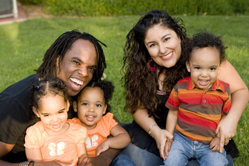 Happy biracial family with triplets at a park.