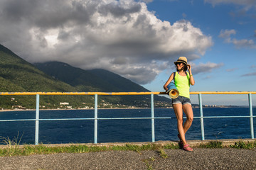 Beautiful woman in straw hat on the pier at the sea, on the background of the coast with mountains