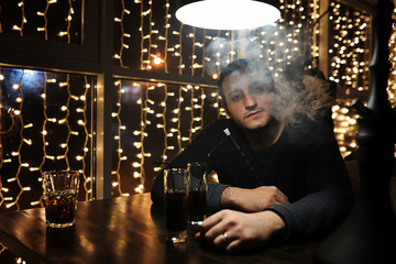 man holding hookah pipe and smoking in a night club