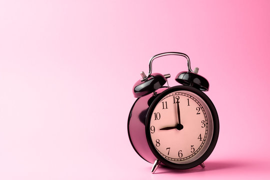black vintage alarm clock on pink color background