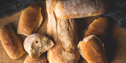Freshly baked bread loaves on burlap dark wooden background. Texture closeup italian bakery products. Top view