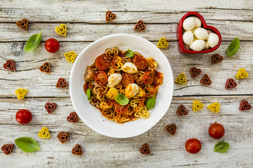 Heart-shaped pasta with tomatoes and basil on wooden background. Italian food.