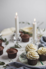 food photo, chocolate muffins and cupcakes white cream in ceramic plates of handwork on a white wooden background with green eucalyptus and baby's breath with candles top view
