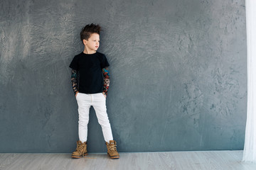 Little fashionable boy on the background of gray walls.