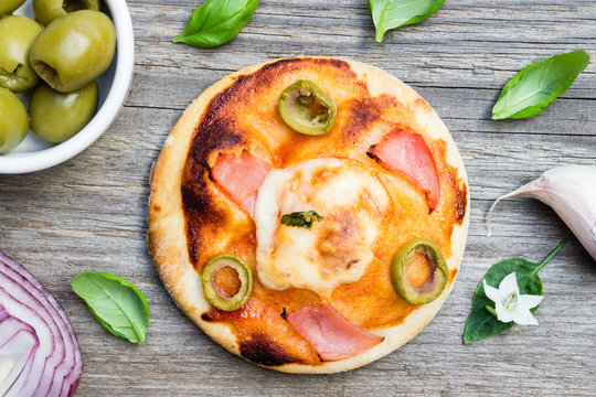 Top View Small Pizza with Ham, Olive and Basil Leaves on Wooden Background