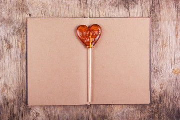 Lollipop in the shape of a heart and an old diary with blank pages. St. Valentine's Day.