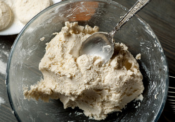 Raw dough in glass bowl with metal spoon in it. Preparation for baking