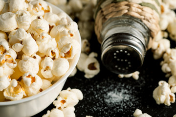 Salt shaker and popcorn in white bowl on a black wooden table