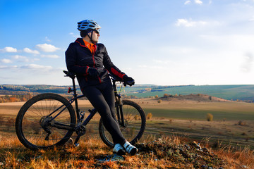 Man in helmet and glasses stay on the bicycle under sky with clouds.