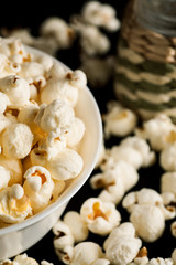 Popcorn in white ceramic bowl with salt shaker on a black wooden table, vertical
