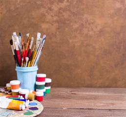 Paints, brushes and palette on the brown wooden background. The workplace of the artist. Banner for school