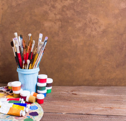 Obraz premium Paints, brushes and palette on the brown wooden background. The workplace of the artist. Banner for school