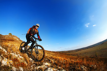 Naklejka na ściany i meble Wide angle view of a cyclist riding a bike on a nature trail in the mountains.