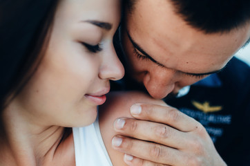 young man kisses on the shoulder of the woman with dark hair close up portrait