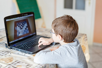 kid boy with glasses playing online chess board game on computer