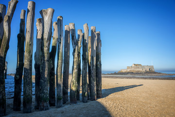 Wood piles at low tide, Fort National in the background, on the beach of Saint Malo, France