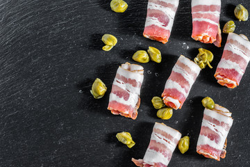 Smoked bacon, rolled meat as tapas or antipasto with capers served on black slate