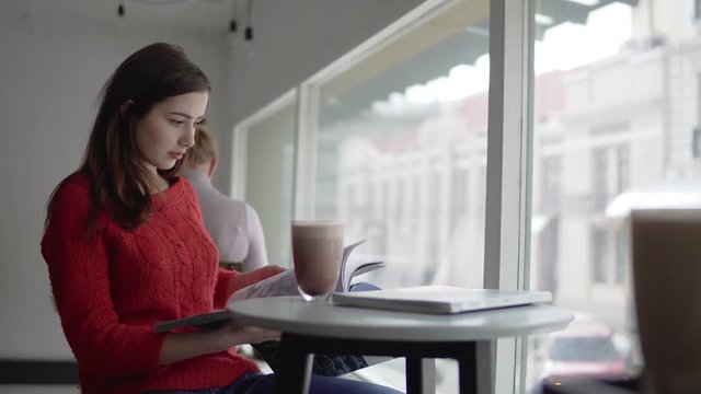Beautiful woman reading newspaper, drinking coffee in cafe