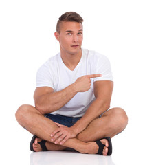 Young Man Sitting Legs Crossed And Pointing