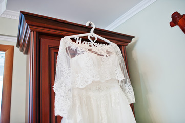 White wedding dress of bride on hangers at closet.