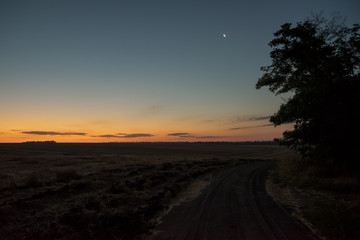 Sunrise in the field. Fantastic sunrise and moon above the field. Dramatic colorful scenery.