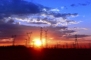 Fototapeta na wymiar Many high voltage towers under the sunset