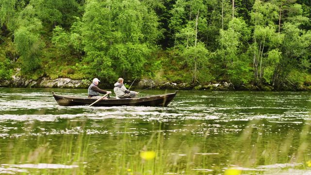 Slow motion dolly shot of senior men rowing boat while fishing on Nordic river
