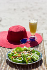Seafood salad, orange fresh juice, hat and sunglasses on the table near sea