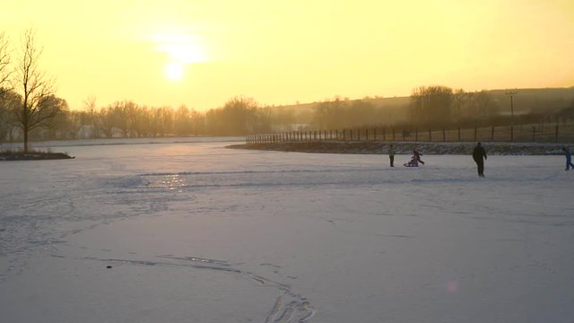 Children ice skating on a pond lake, sunset evening with snow