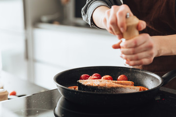 Cropped image of young woman cooking fish and tomatoes.