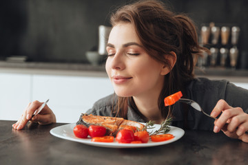 Young woman eating fish and tomatoes.